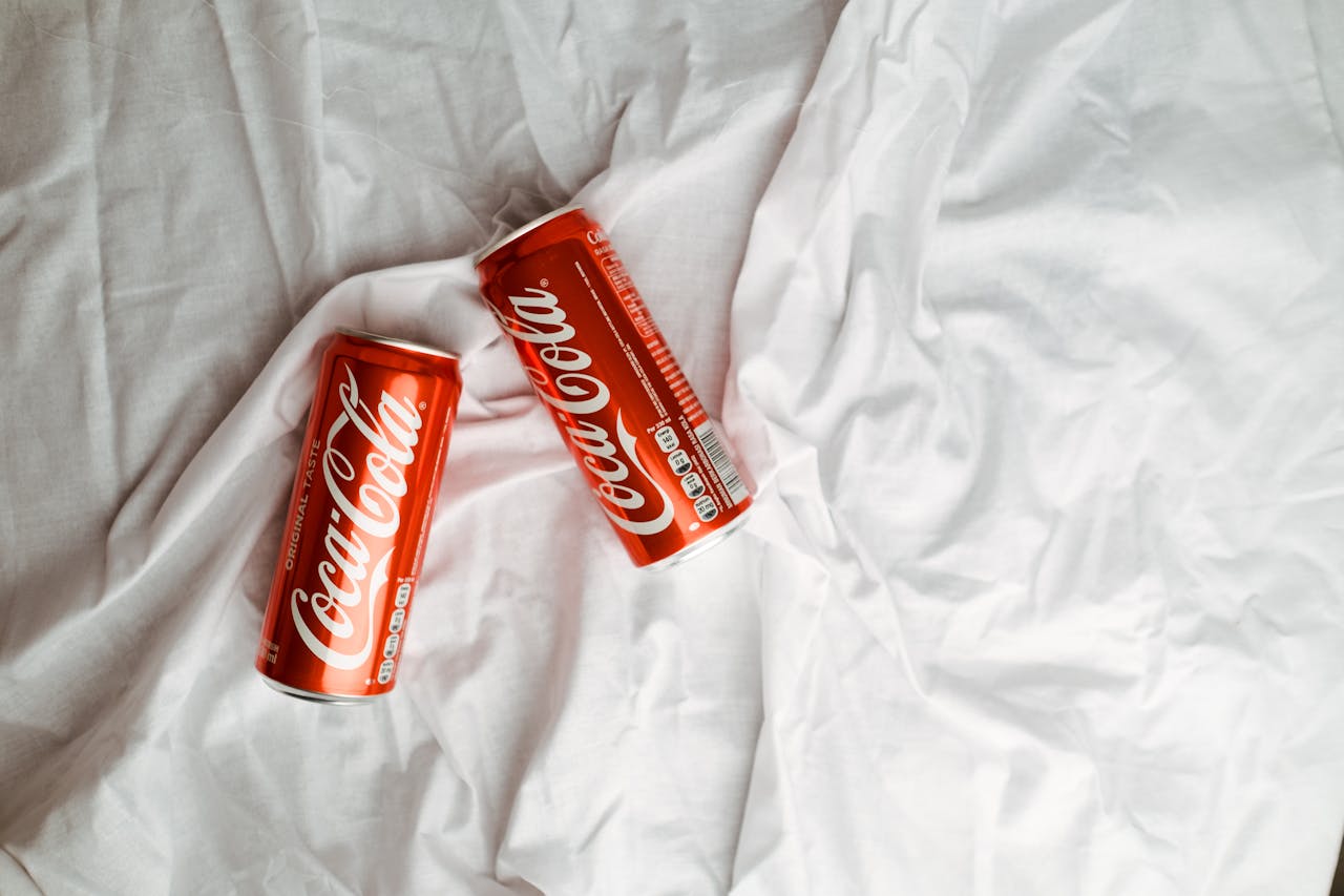 Mastering the First Impression: Your intriguing post title goes here Two Coca Cola cans placed on a crumpled white textile, showcasing a classic beverage design.